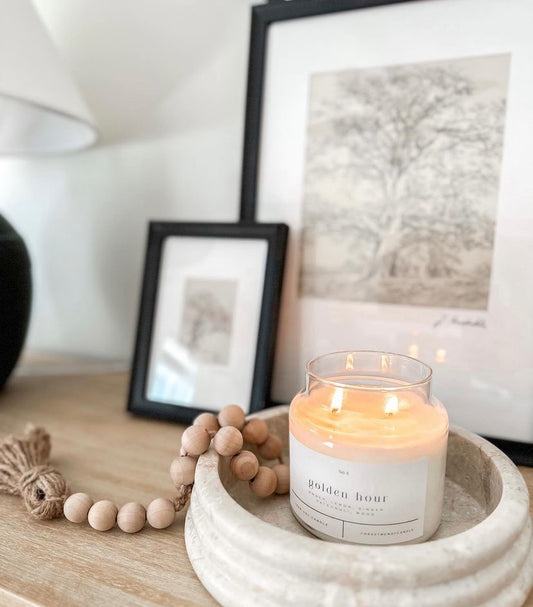golden hour soy candle burning on modern organic entryway table next to picture frames with vintage art and a distressed lamp