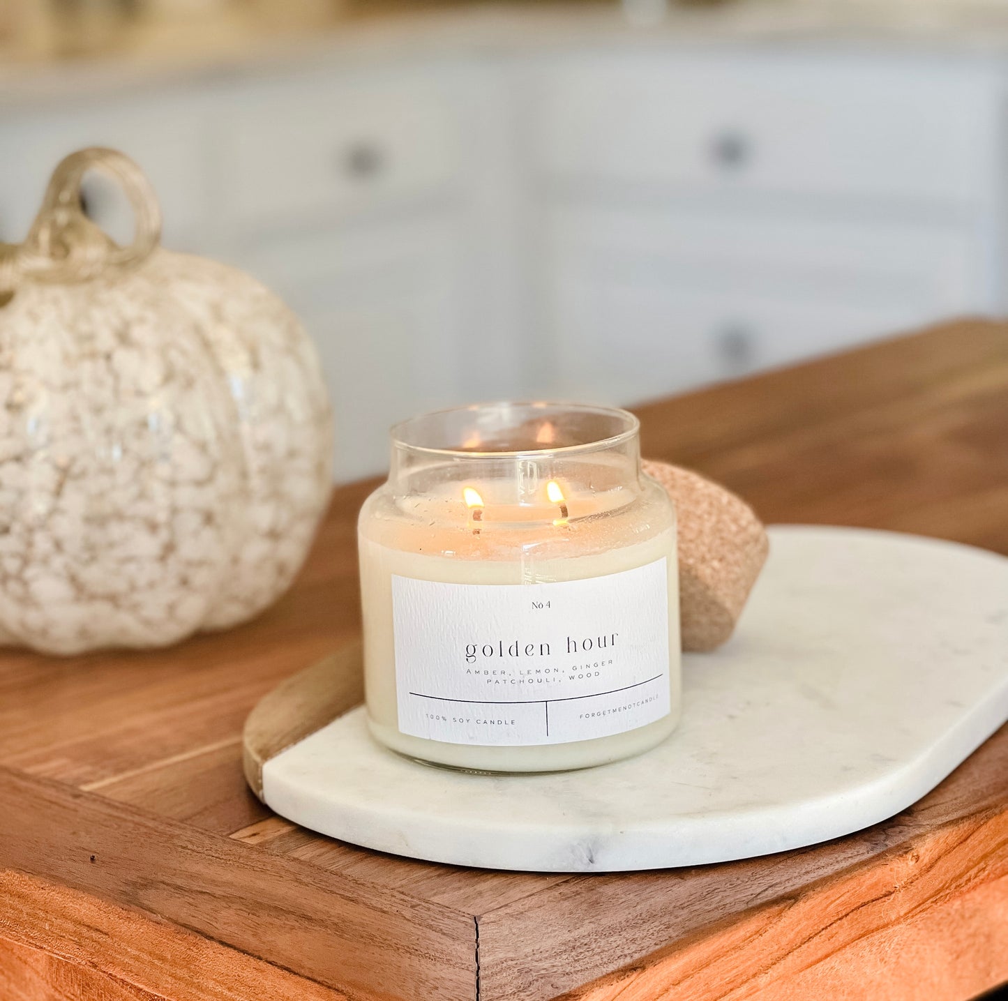 Golden Hour 100% soy wax candle with cork lid, lit and displayed on a marble tray in a cozy, autumn-themed setting. Hand-poured, eco-friendly candle with warm notes of amber, lemon, ginger, patchouli, and wood for clean, non-toxic home fragrance.