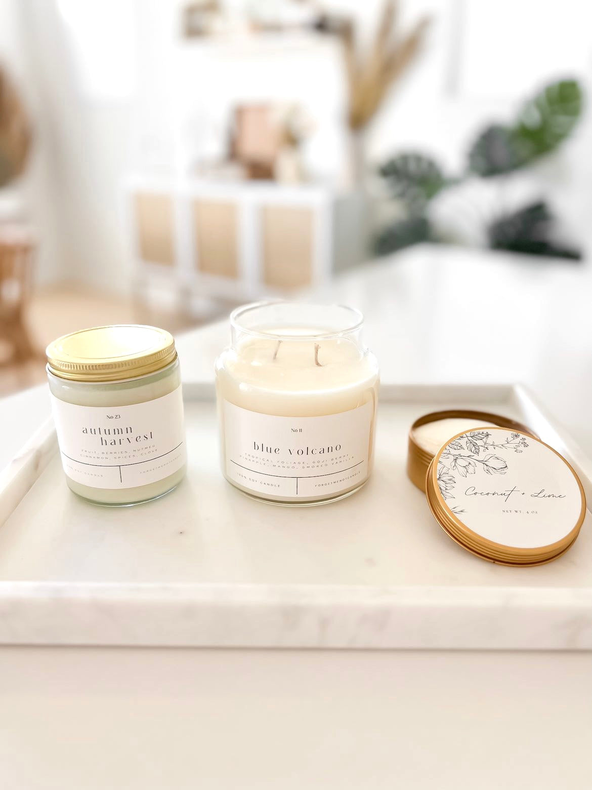 Autumn Harvest and Blue Volcano 100% soy wax candles displayed on a white marble tray alongside a Coconut Lime travel tin. Hand-poured, eco-friendly candles featuring seasonal and tropical scents, perfect for clean, non-toxic home fragrance and modern decor.